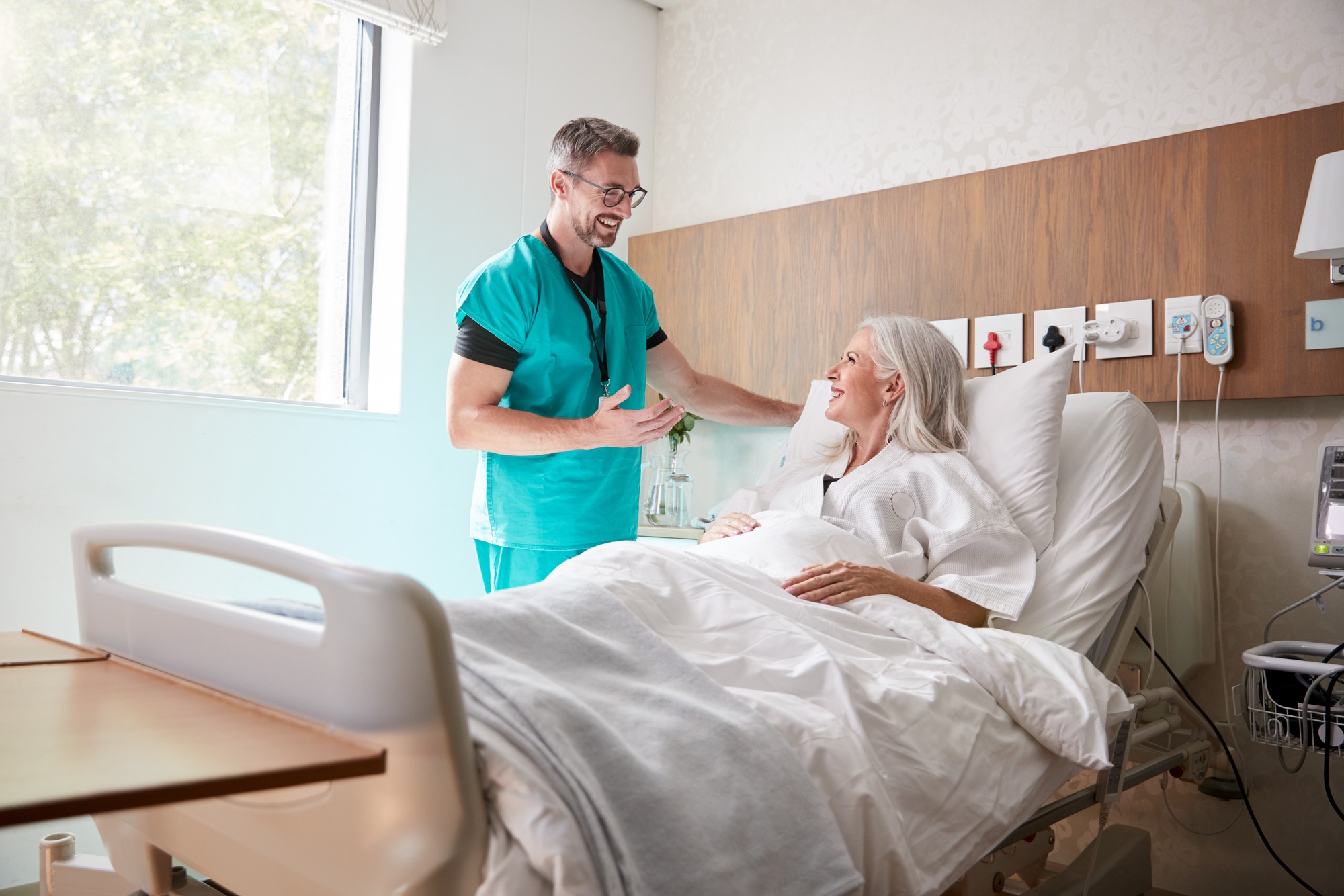 A healthcare worker smiles and interacts with a smiling patient in a hospital room, fostering a supportive environment during recovery.