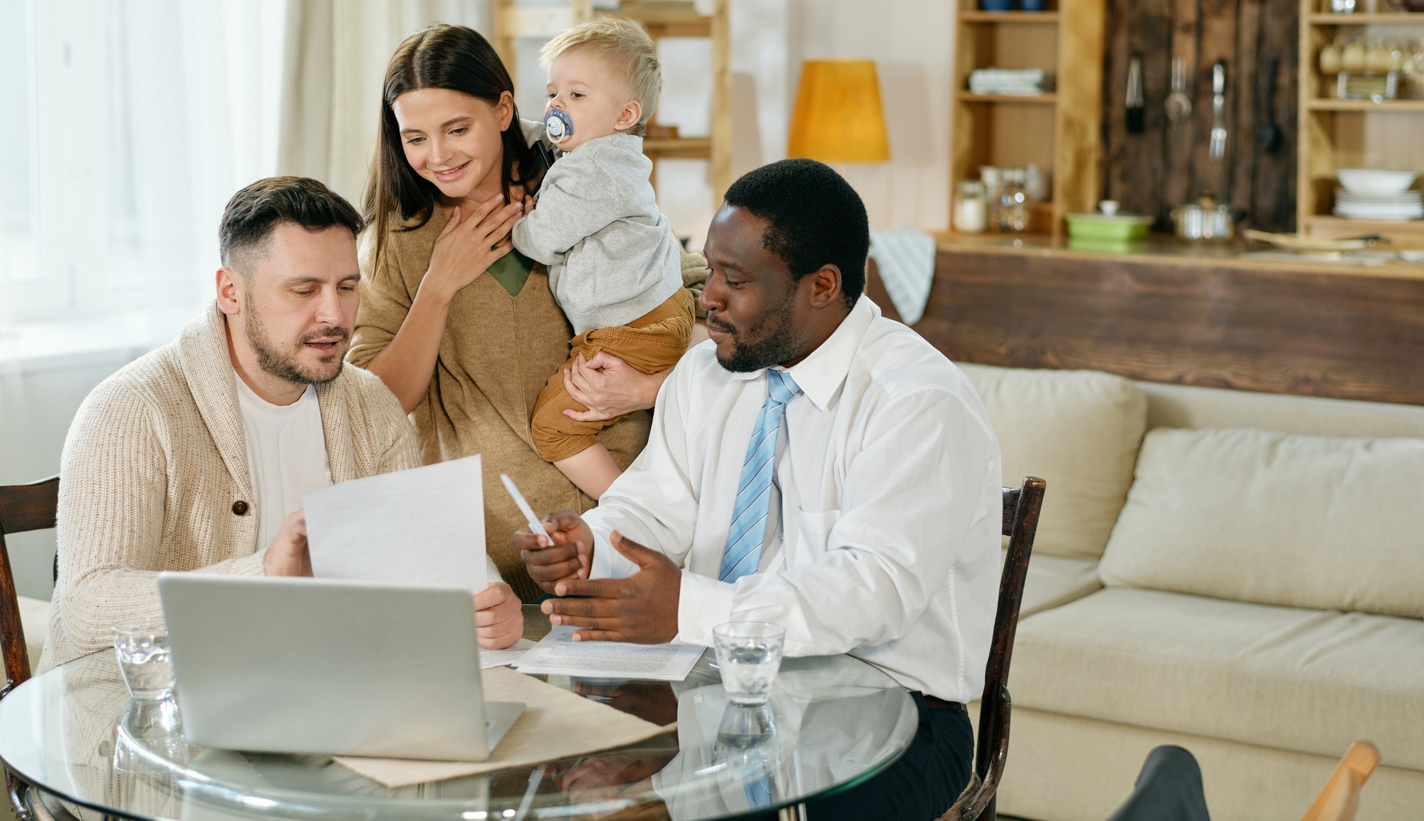 A family meets with a financial advisor at a dining table, discussing important documents while a child is held by the mother.